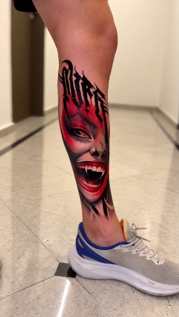 Tatuagem trash polka de rosto feminino com presas e lettering na perna, feita por Lucas Mares Guia em Vila Velha